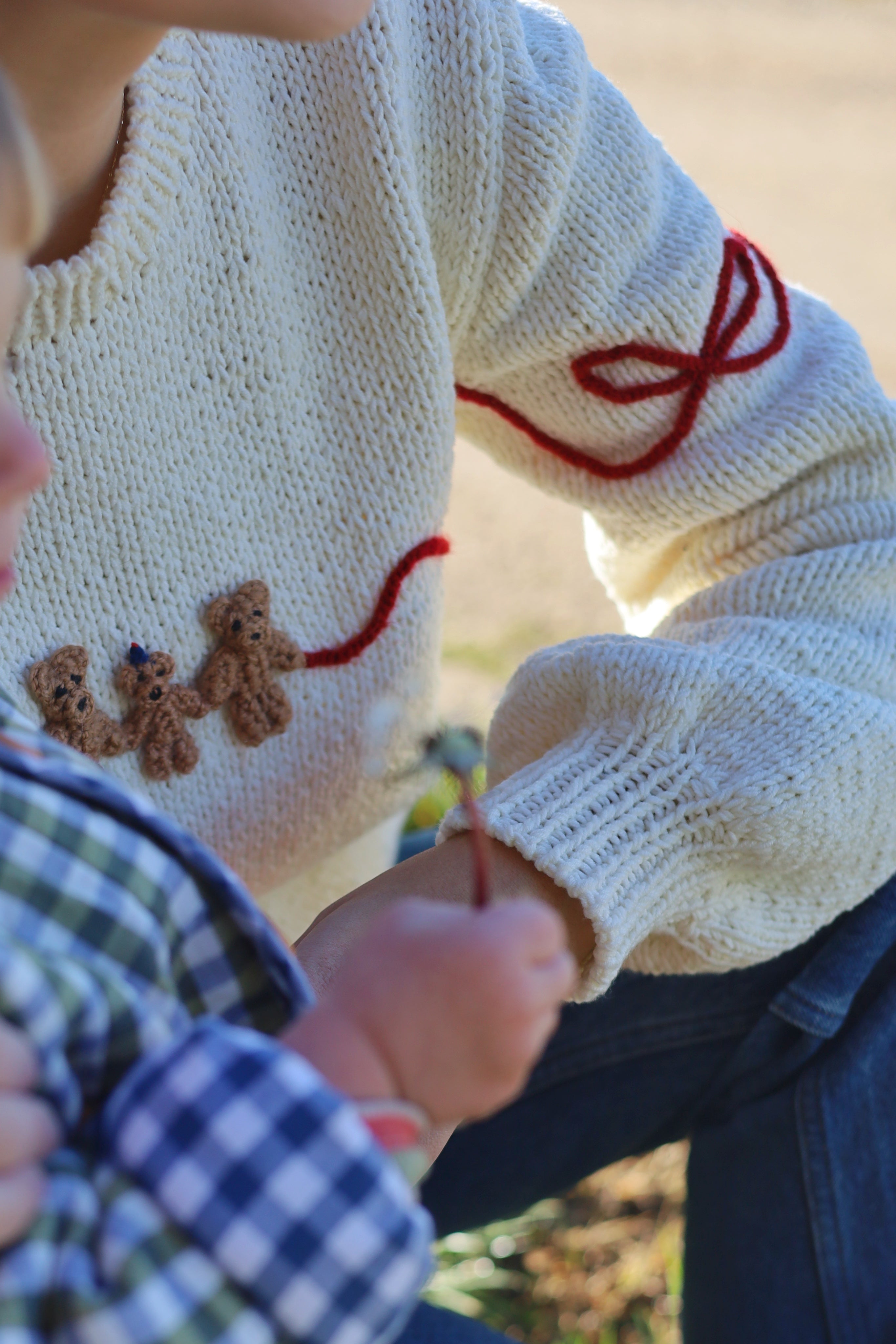 Beige hand knitted sweater with embroidered red bows and three bears.